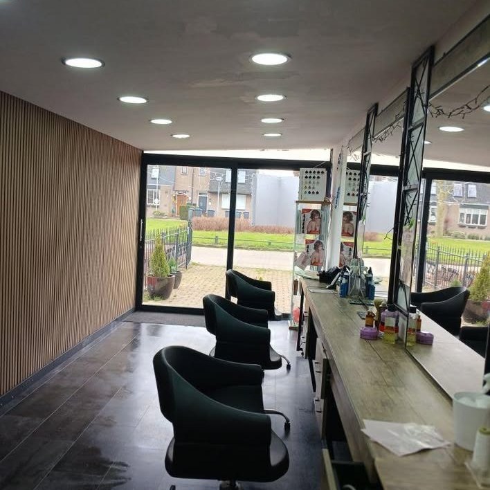 Haarmode Rosa in Lelystad: groene stoelen, houten werkblad en de glazen pui